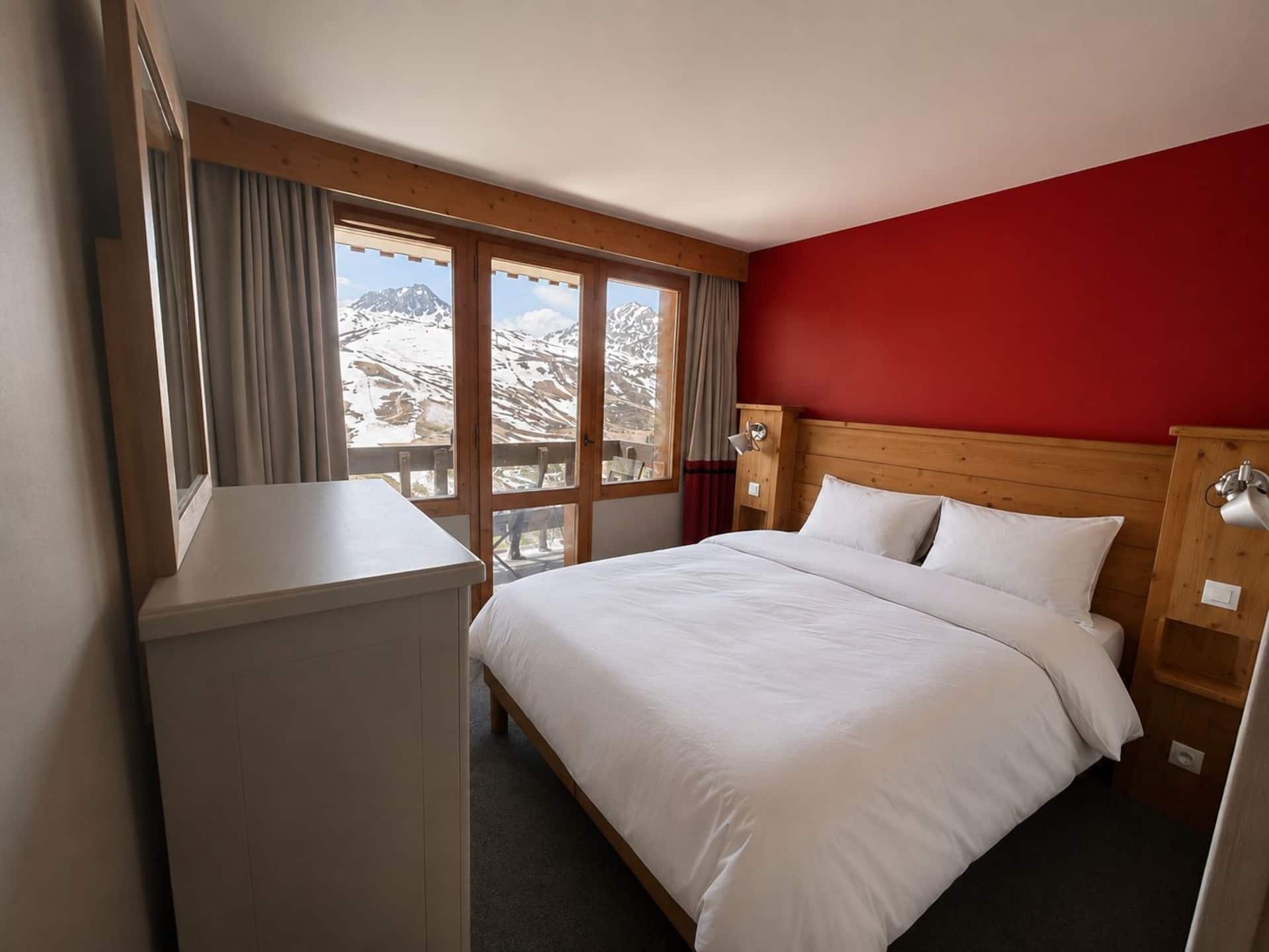 Chambre avec lit double face à une baie vitrée ouverte sur les montagnes